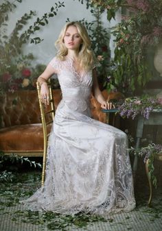 a woman in a white dress sitting on a chair next to flowers and greenery