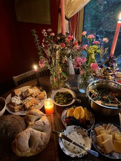 a table full of food with candles and flowers in the window sill behind it