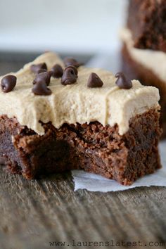 two pieces of chocolate cake with frosting and chocolate chips on top, sitting on a wooden table