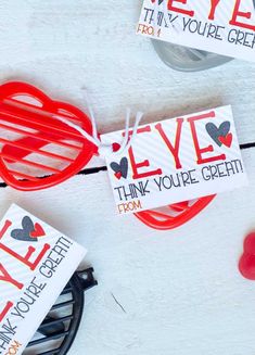 valentine's day cards and sunglasses on a white table with red candies around them