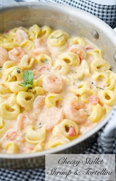 a skillet filled with pasta and shrimp on top of a checkered table cloth