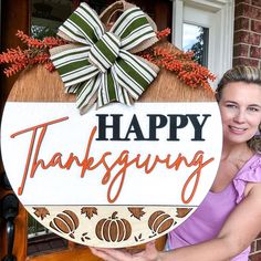 a woman holding a happy thanksgiving sign in front of a door with a bow on it