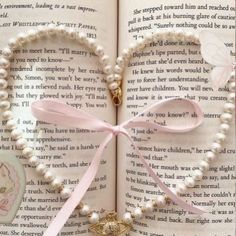 a heart shaped book with pearls and a pink ribbon on it's cover, sitting in front of an open book