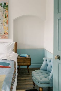 a bedroom with a blue chair next to a bed and a painting on the wall