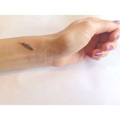 a woman's arm with a small feather tattoo on it