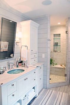 a white bathroom with two sinks and a large mirror over the bathtub, along with a walk in shower