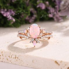 an opal and diamond ring sits on top of a white marble slab with purple flowers in the background