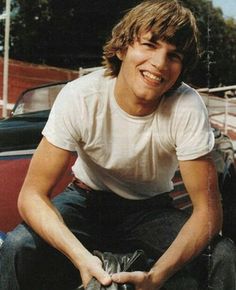 a young man sitting on the hood of a car with his hands in his pockets