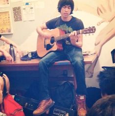 a man sitting on top of a wooden table holding a guitar in front of him