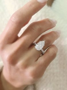 a woman's hand with a diamond ring on her finger and a white sweater in the background