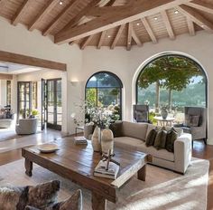 a living room filled with lots of furniture next to a large open window covered in wooden beams