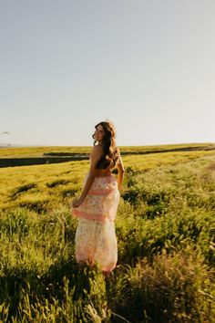 a woman standing in the middle of a field with her hair blowing in the wind