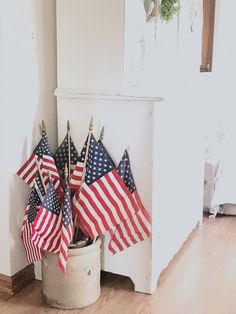 several american flags are placed in a bucket on the floor next to a white fireplace