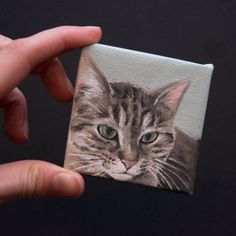 a hand holding up a small painting of a cat