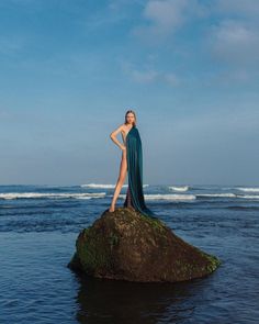 a woman standing on top of a rock in the ocean