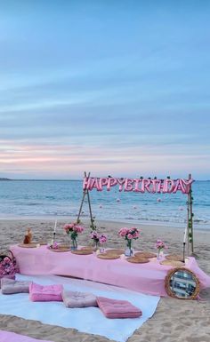 a birthday party setup on the beach with pink and white decorations, flowers and candles