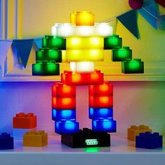 an illuminated building made out of legos on top of a white table next to a window