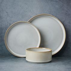 two white and gold dinner plates next to each other on a gray surface with a grey wall in the background