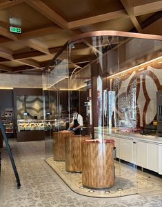 the interior of a restaurant with glass walls and wood accents on the ceiling, along with large round wooden stools