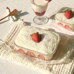 two desserts with strawberries on top are sitting on a white tablecloth next to glasses and utensils