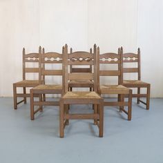 six wooden chairs sitting side by side against a white wall with no one in it