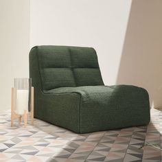 a green chair sitting on top of a tiled floor next to a vase with flowers