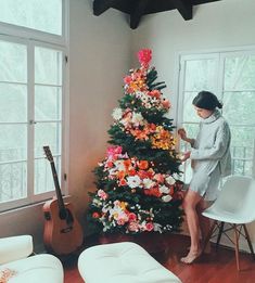 a woman sitting on a chair next to a christmas tree with flowers in the corner