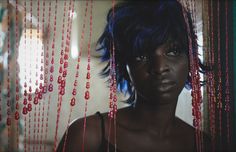 a woman with blue hair and red beads hanging from her head is staring at the camera