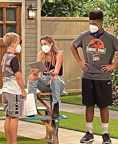 three people wearing face masks standing in front of a house