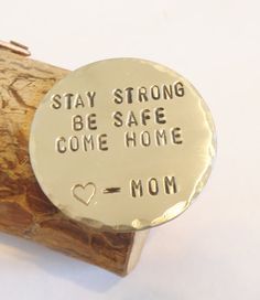 a silver charm that says stay strong be safe come home mom sitting on top of a piece of wood