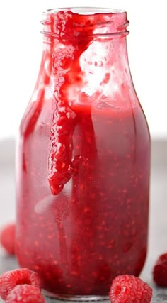 raspberry sauce in a glass jar with fresh raspberries around the edges