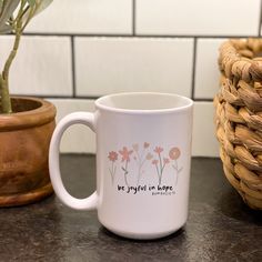 a white coffee mug sitting on top of a counter next to a potted plant