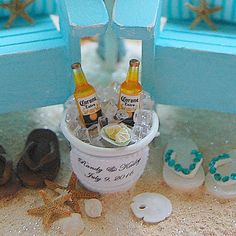 two bottles of beer sit in a bucket on the sand next to sandals and starfish