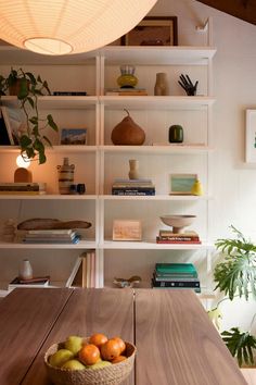 a wooden table topped with a bowl of fruit next to a shelf filled with books