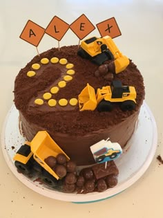 a chocolate cake decorated with construction vehicles and nameplates on the top, sitting on a plate