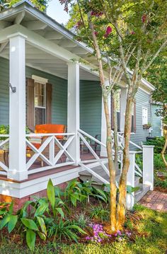 a small blue house with white trim and porch railings on the front steps, surrounded by lush greenery