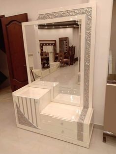 a large white mirror sitting on top of a floor next to a wooden table and chair