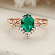 an oval green stone surrounded by white diamonds on top of a pink gold wedding ring