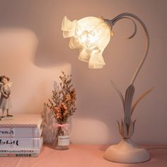 a lamp that is sitting on top of a table next to some books and flowers