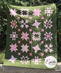 a green quilt with pink and white stars hanging from it's side on a stone wall