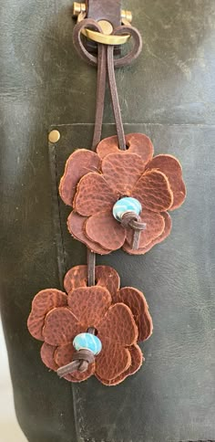 a handbag with two flowers attached to the front and side of it, hanging from a leather strap