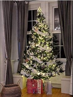 a decorated christmas tree in front of a window with presents under it and lights on