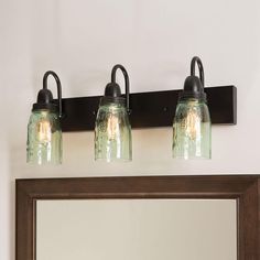 three mason jar lights are mounted on the wall above a mirror and vanity light fixture