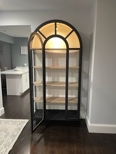 an arched glass display case in the corner of a room with hardwood floors and white walls