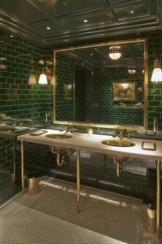 a green tiled bathroom with two sinks and mirrors