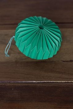 a green paper fan sitting on top of a wooden table next to a piece of string