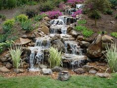 a small waterfall surrounded by rocks and flowers