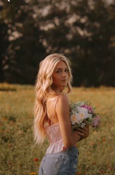 a beautiful young blond woman holding a bouquet of flowers in a field with wildflowers