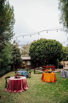 an outdoor dining area is set up with colorful table cloths and chairs, surrounded by trees