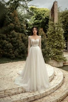 a woman in a wedding dress standing on a stone path with trees and bushes behind her